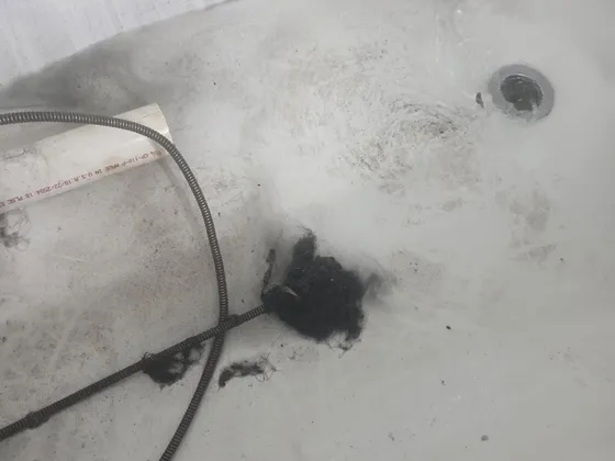 A drain cable pulling a clump of hair and debris out of a bathtub drain