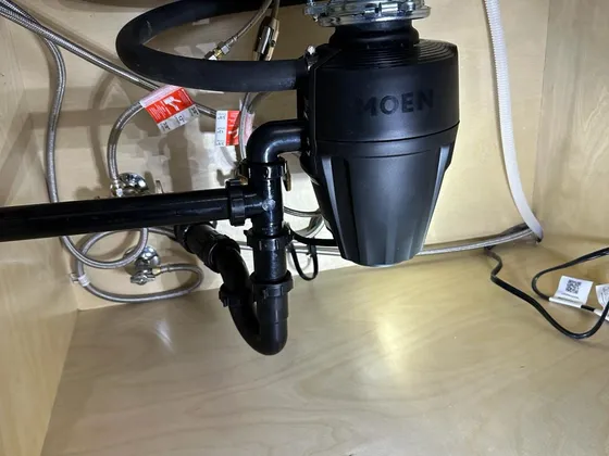 The drain under a kitchen sink: garbage disposal, black trap and dishwasher hose