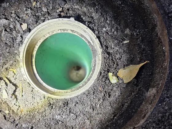 An open sewer cleanout in the ground, looking down into the drain line
