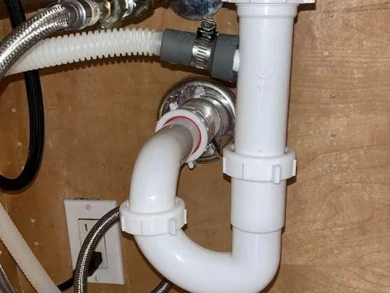 A white P-trap and drain line under a sink, beside the supply valves